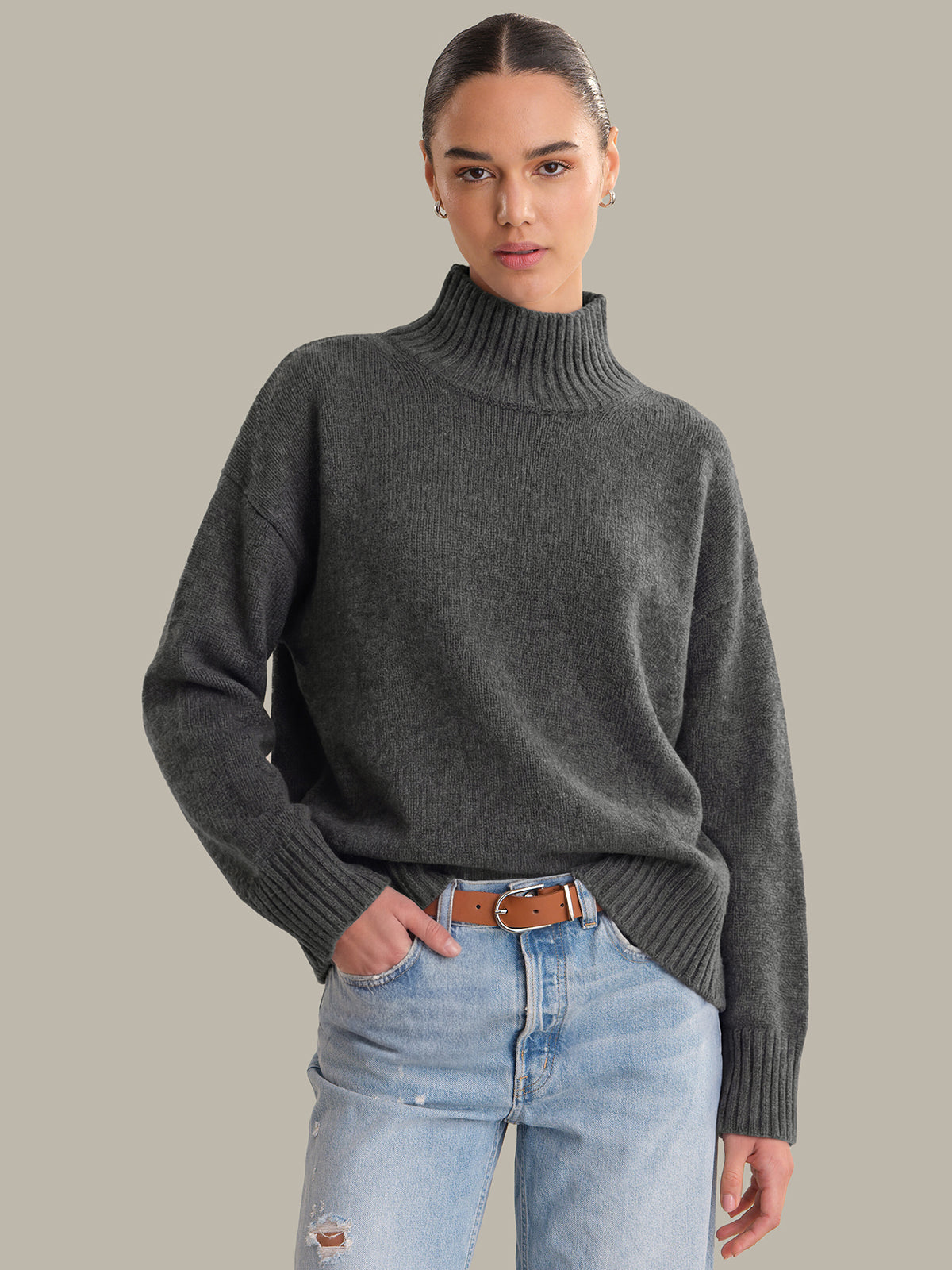 Person wearing a gray turtleneck sweater and light blue jeans on a plain background