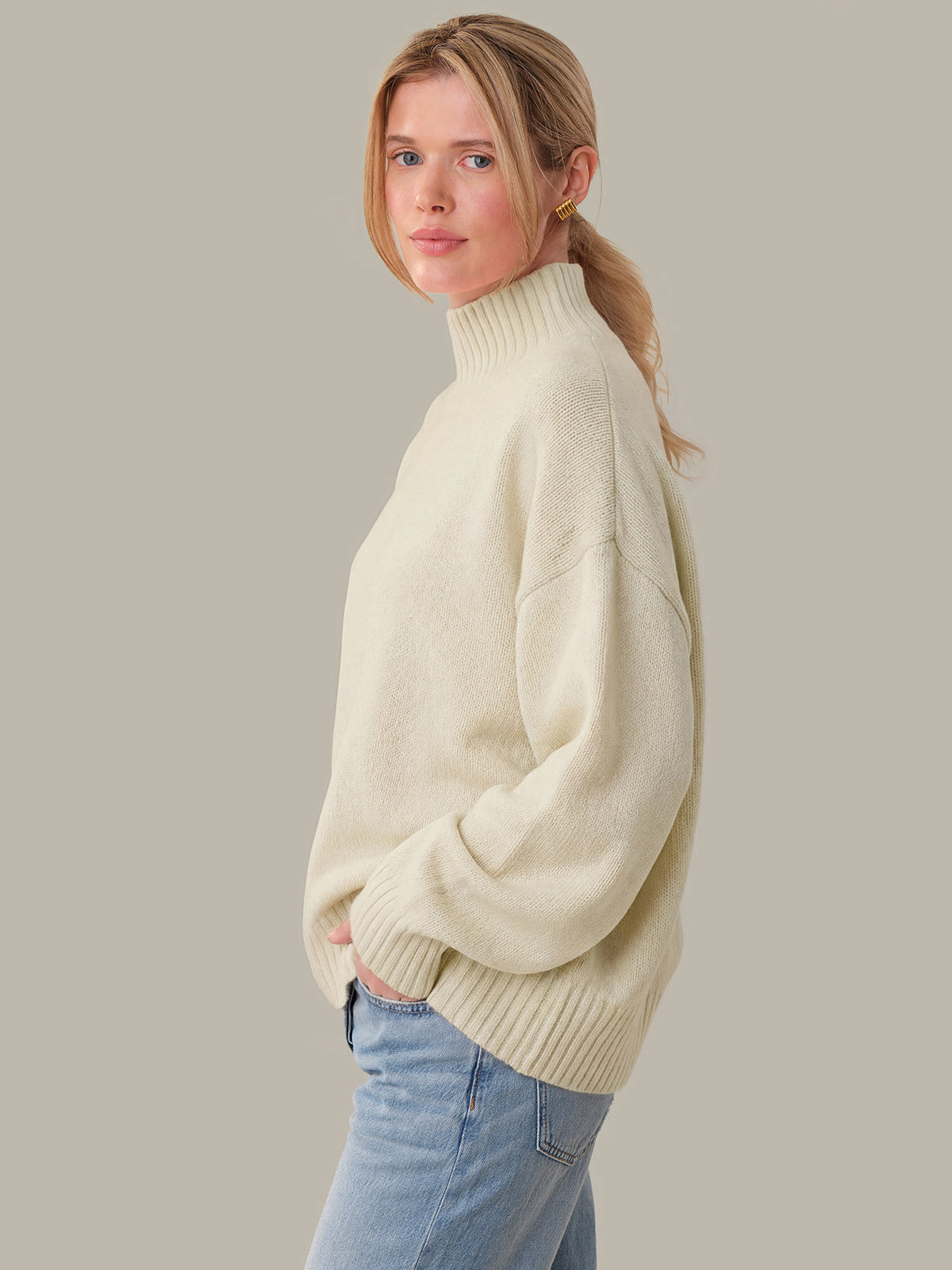 Woman wearing a cream sweater and blue jeans against a plain background