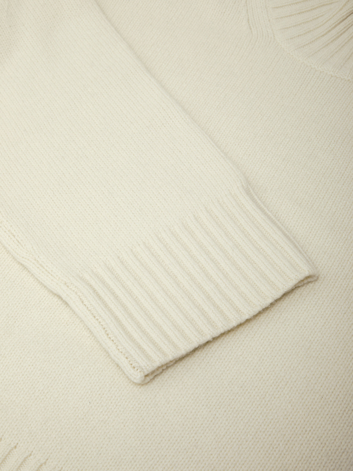 Close-up of a cream-colored sweater with ribbed texture on a matching background