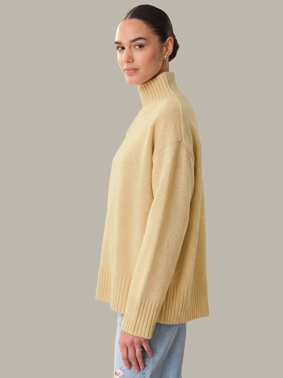 Woman wearing a beige turtleneck sweater against a neutral background