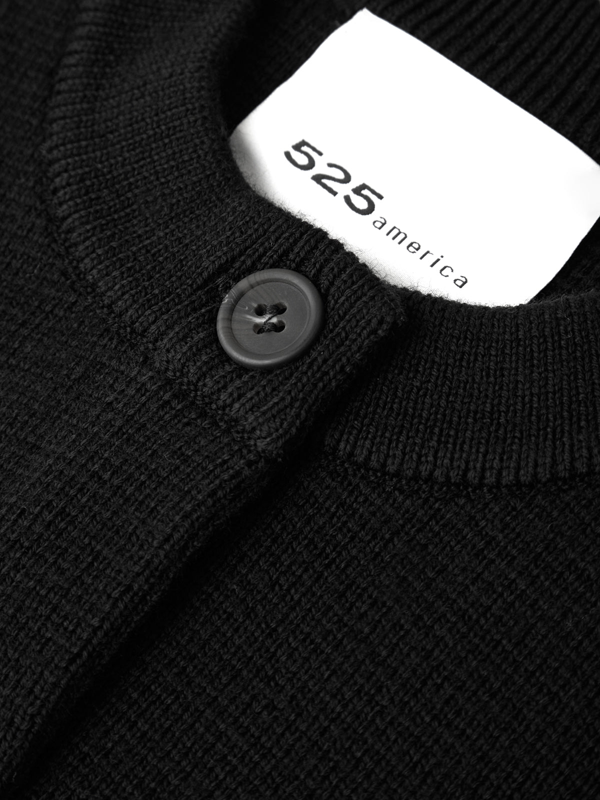 Close-up of a black sweater with a button and a white label displaying '525 america'.