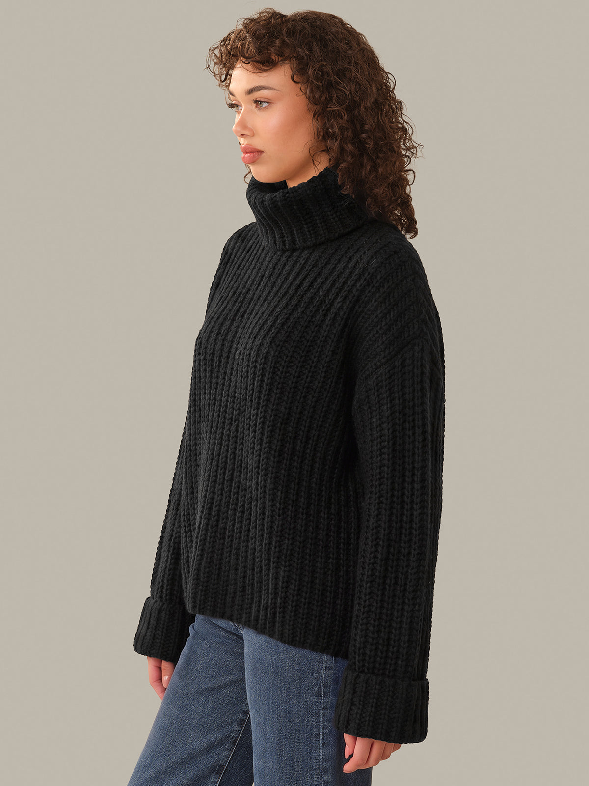 Woman wearing a black turtleneck sweater and blue jeans on a neutral background