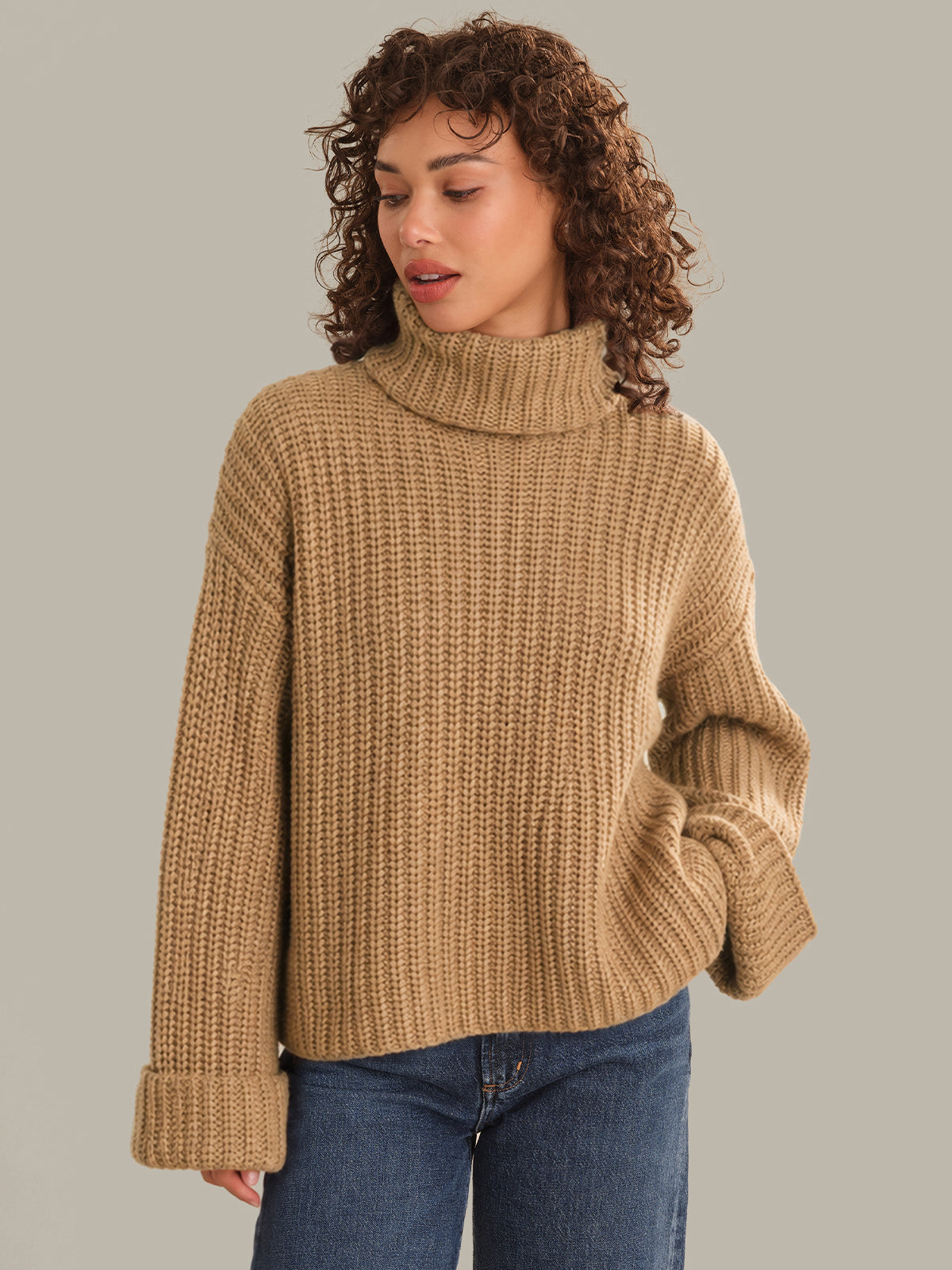 Woman wearing a beige knitted sweater against a plain background
