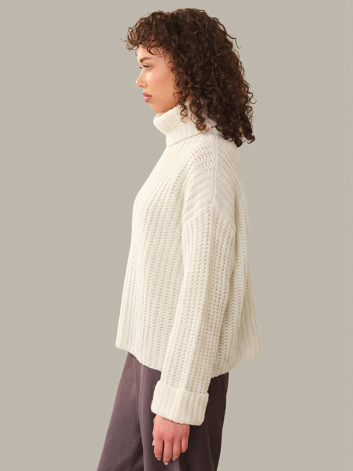 Person wearing a white ribbed sweater against a plain background