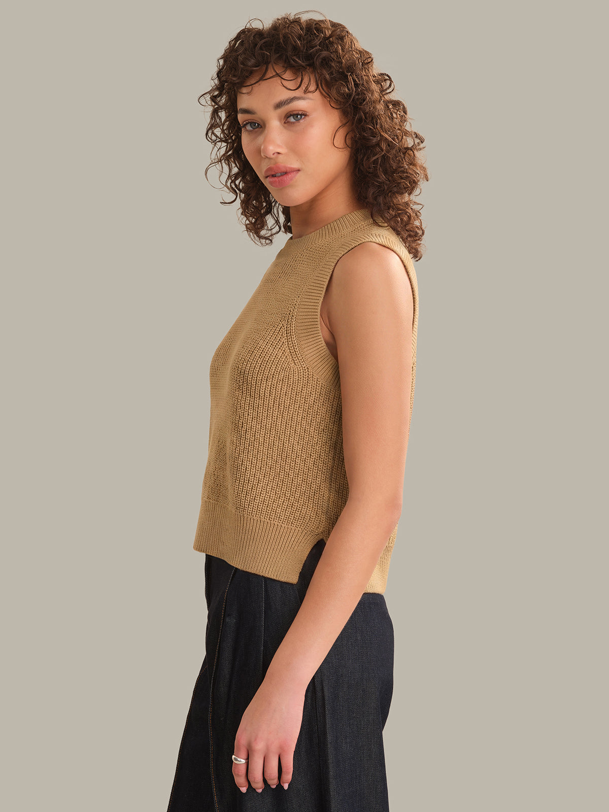 Woman wearing a beige sleeveless knitted top against a plain background