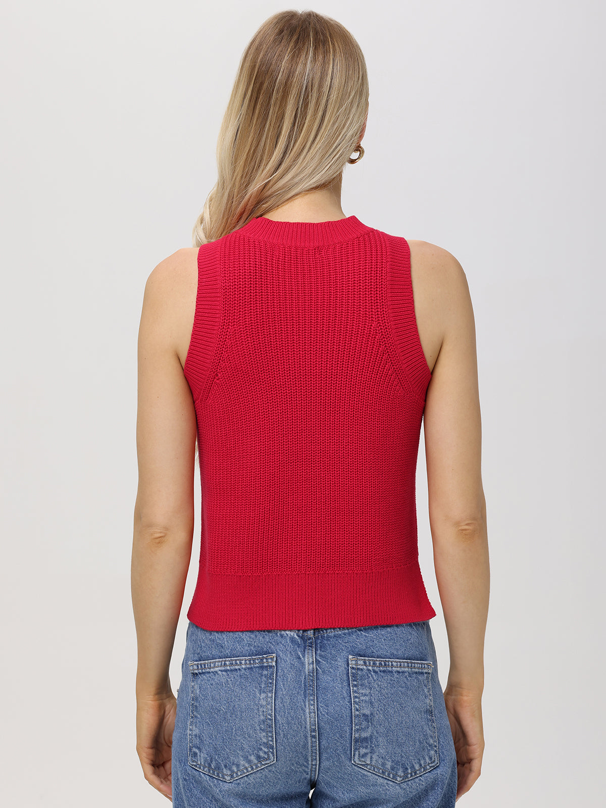 A person with long, light blonde hair stands with their back to the camera, wearing a sleeveless red 100% cotton knit top from 525 America and blue jeans, embodying chic simplicity against a plain light background.