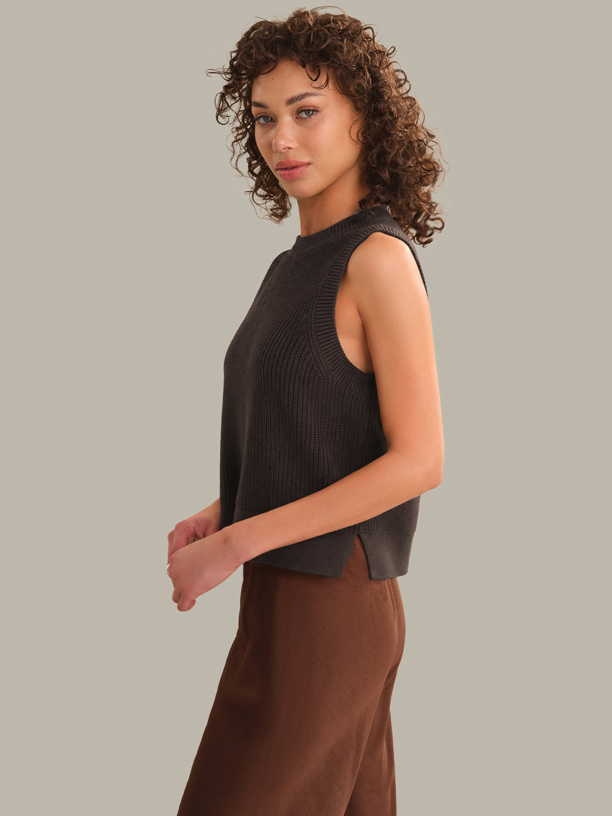 Woman wearing a brown sleeveless top and brown pants against a gray background