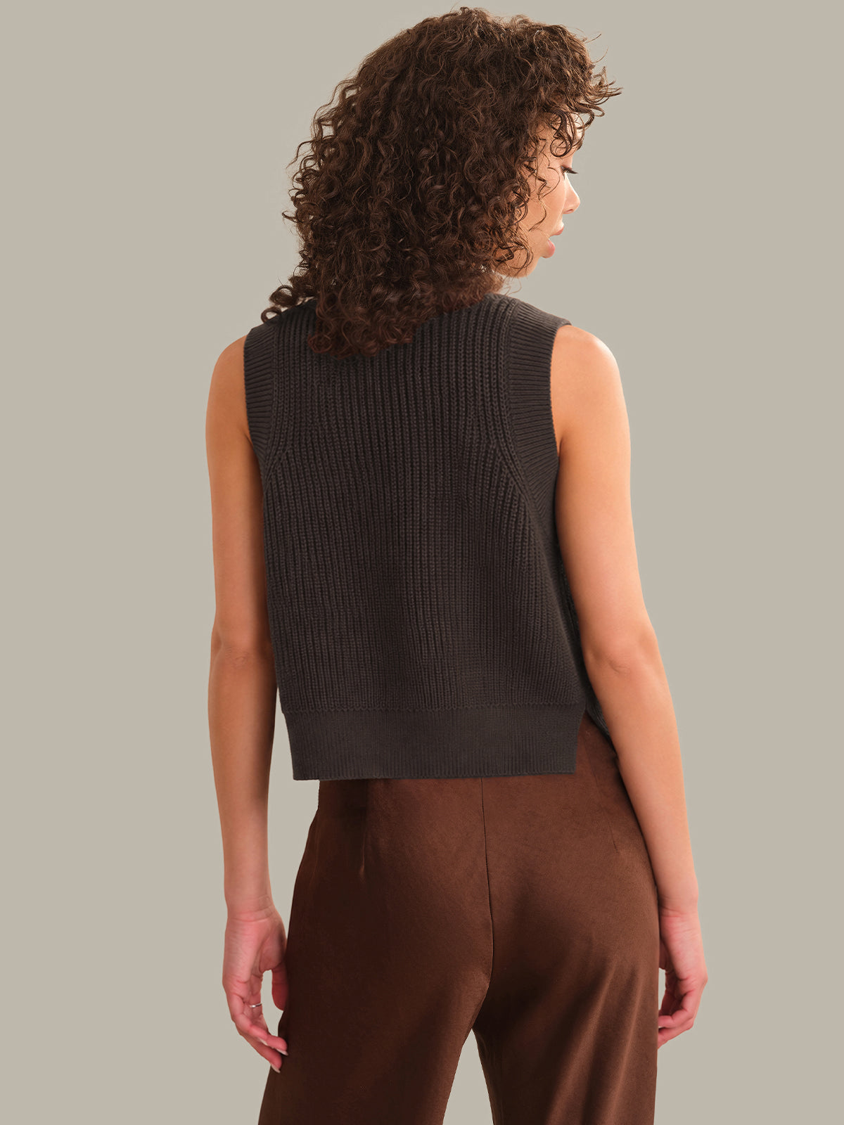 Woman wearing a brown sleeveless knitted top and brown pants against a plain background
