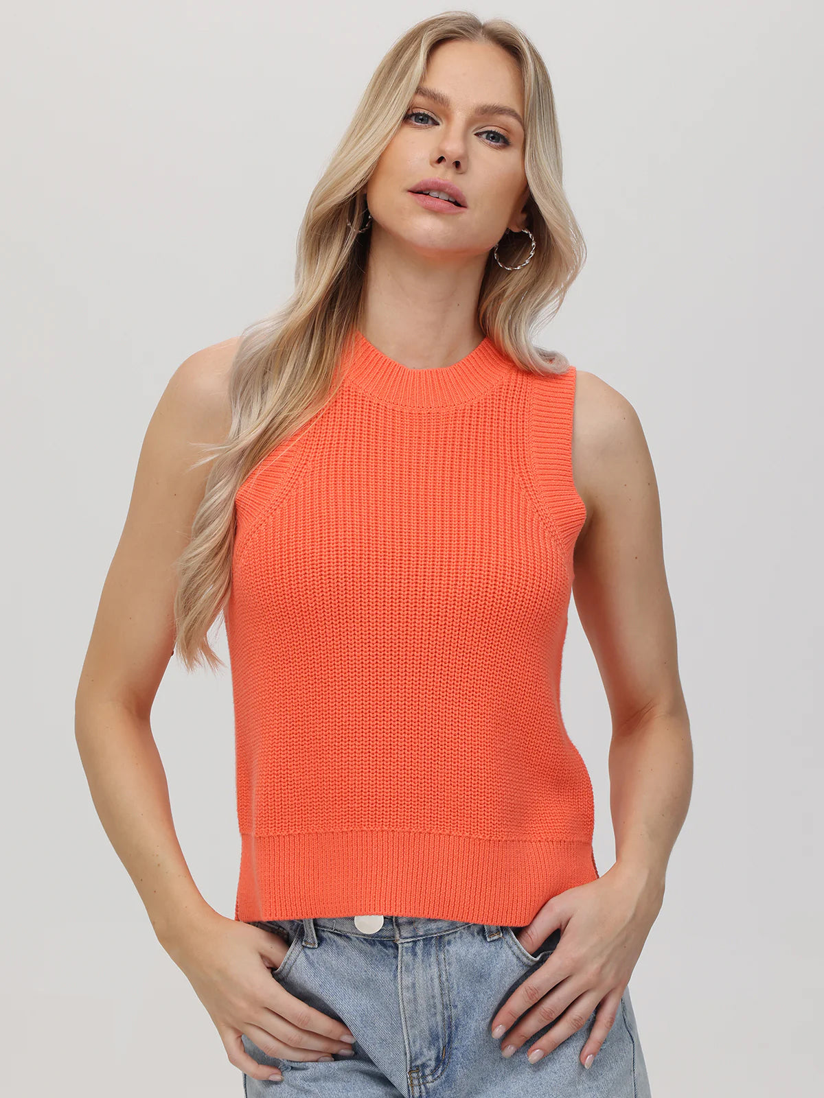 Woman wearing an orange sleeveless knitted top against a plain background