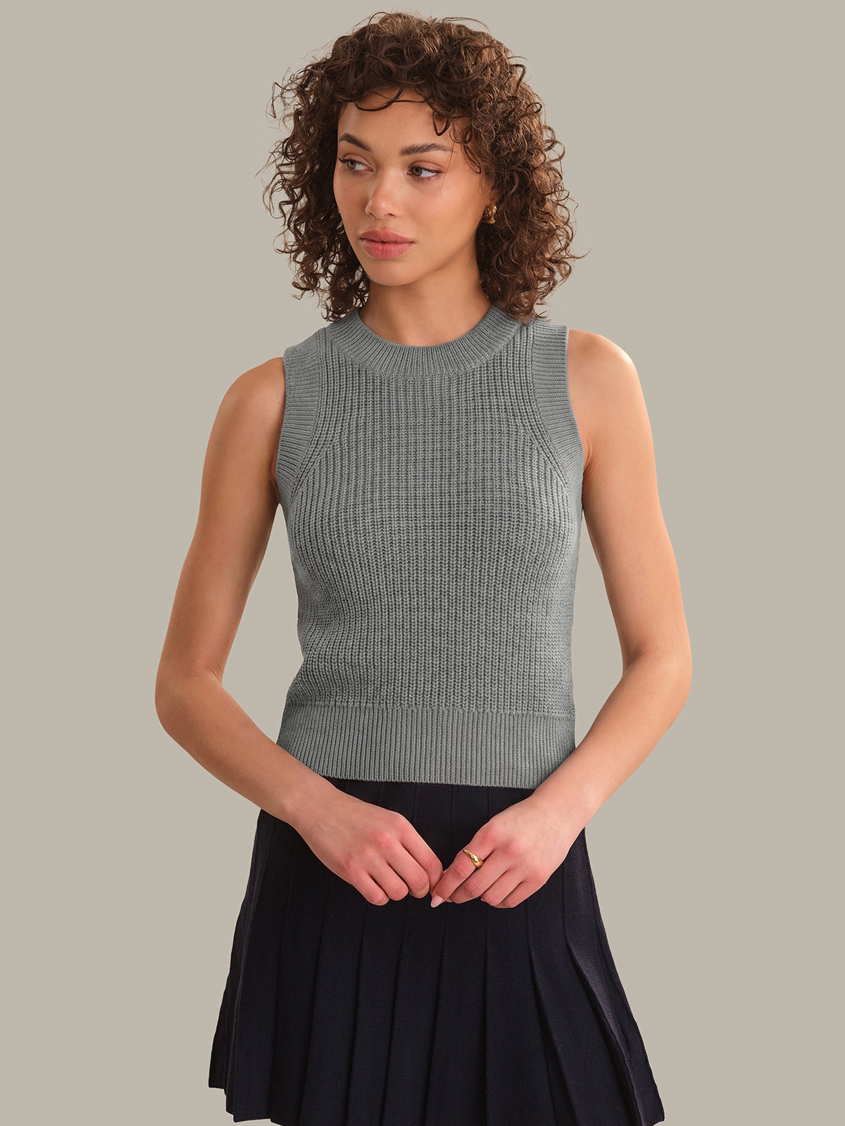 Woman wearing a gray sleeveless knitted top and black skirt against a plain background