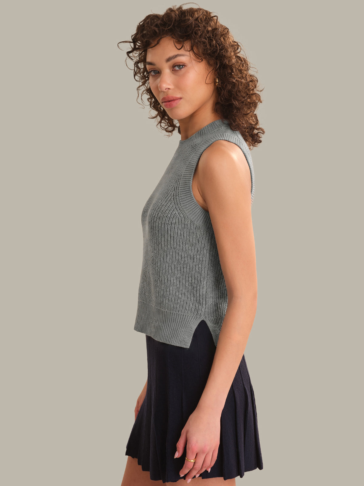 Woman wearing a sleeveless gray knit top and black skirt on a plain background