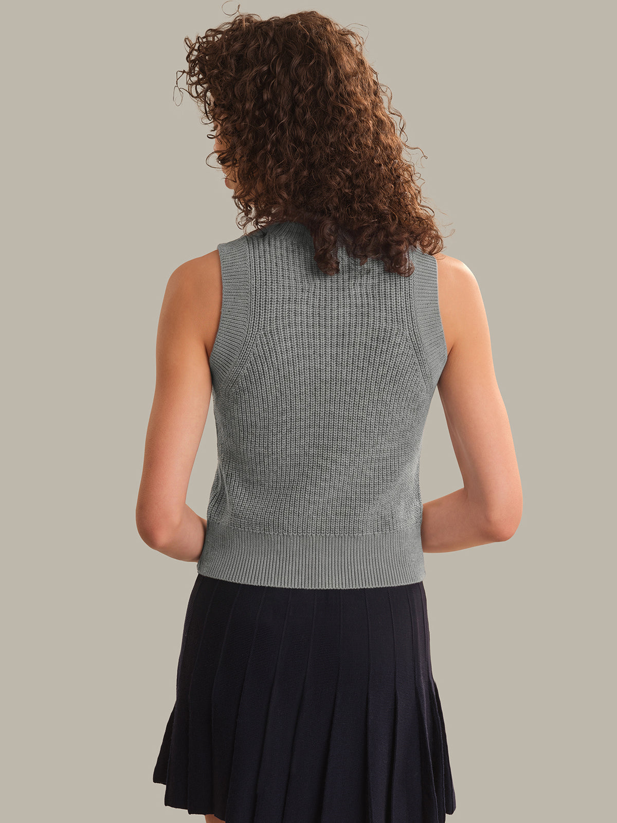 Woman wearing a gray sleeveless knitted top and black skirt on a plain background