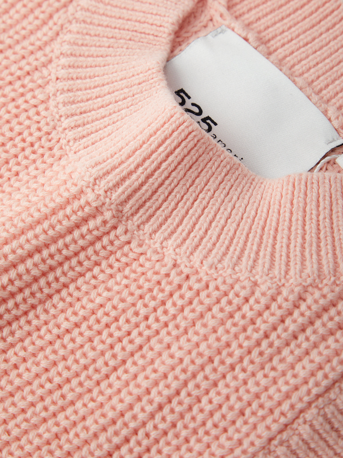 Close-up of a pink knitted sweater with a brand tag.