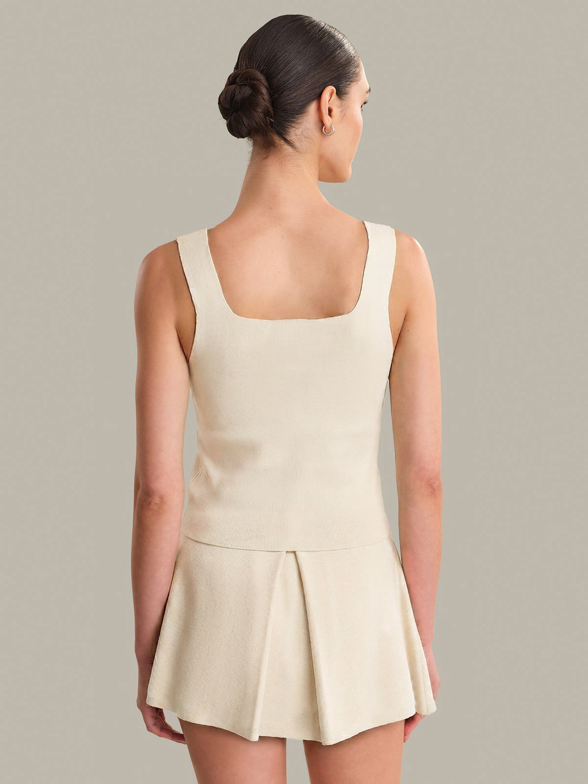 Woman wearing a beige tank against a plain background
