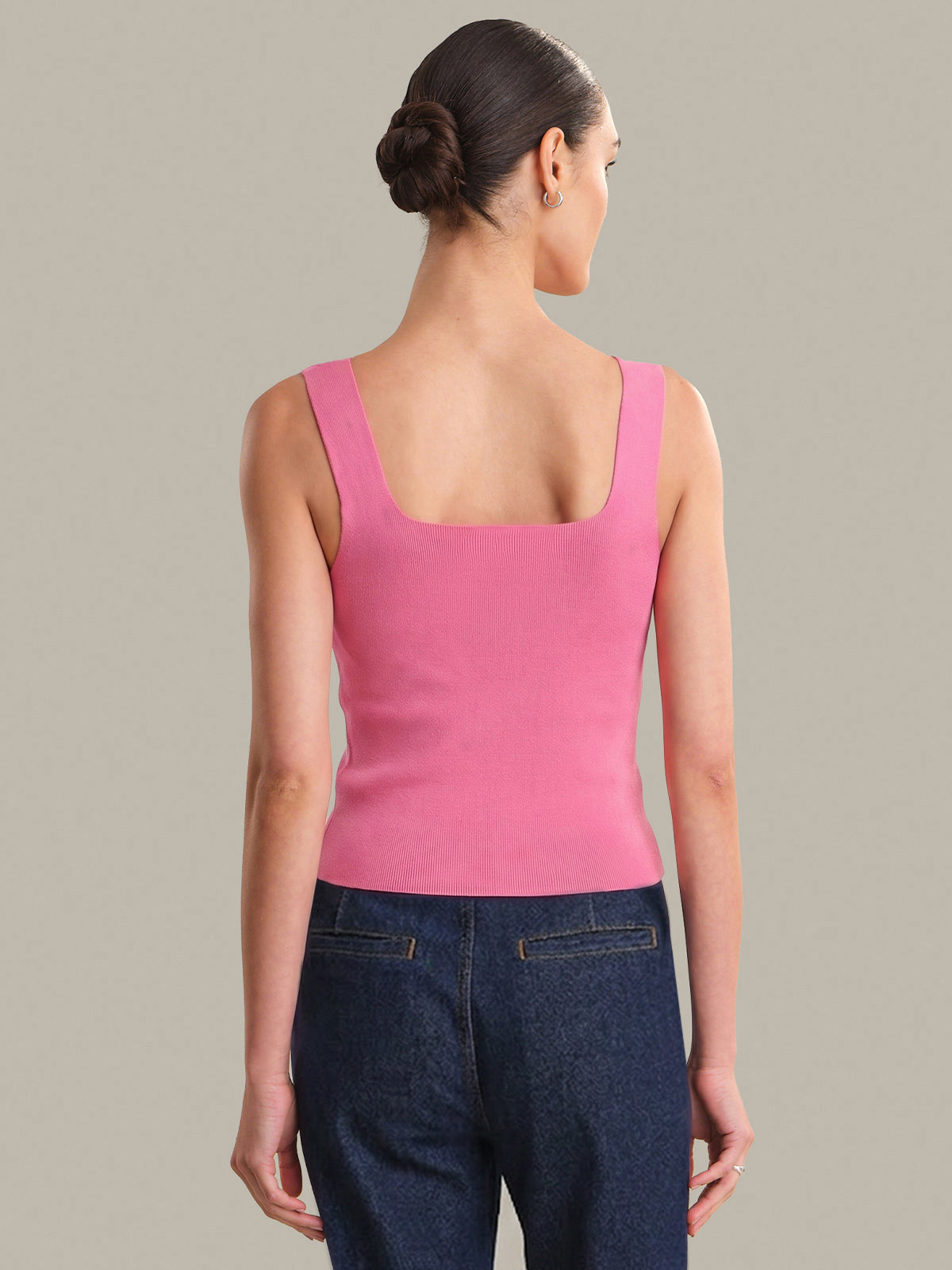 Woman wearing a pink tank top and blue jeans against a neutral background