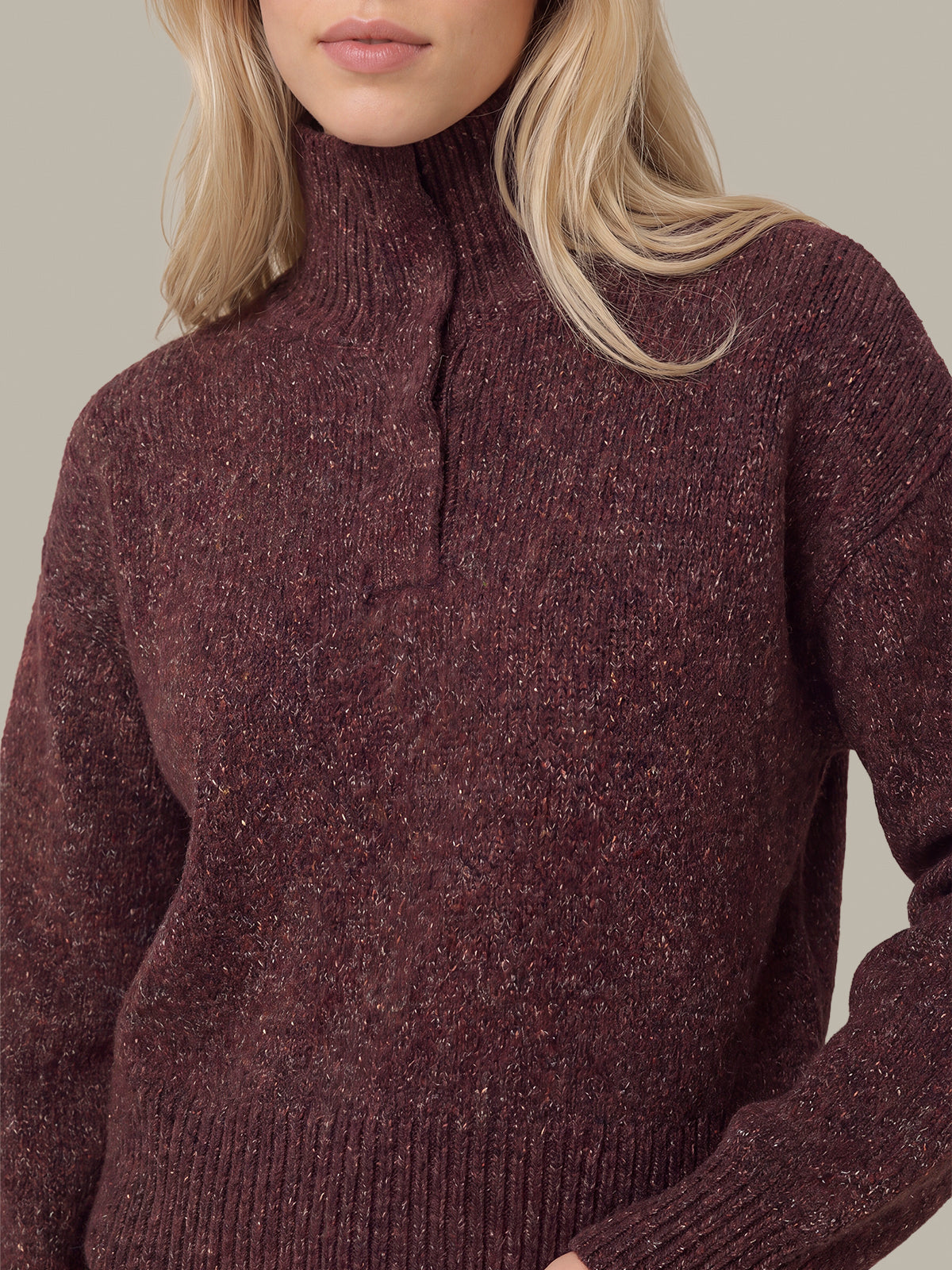A close-up of a woman wearing a ribbed turtleneck sweater in a heathered burgundy-brown color, showing her blonde hair and the texture of the knit fabric.