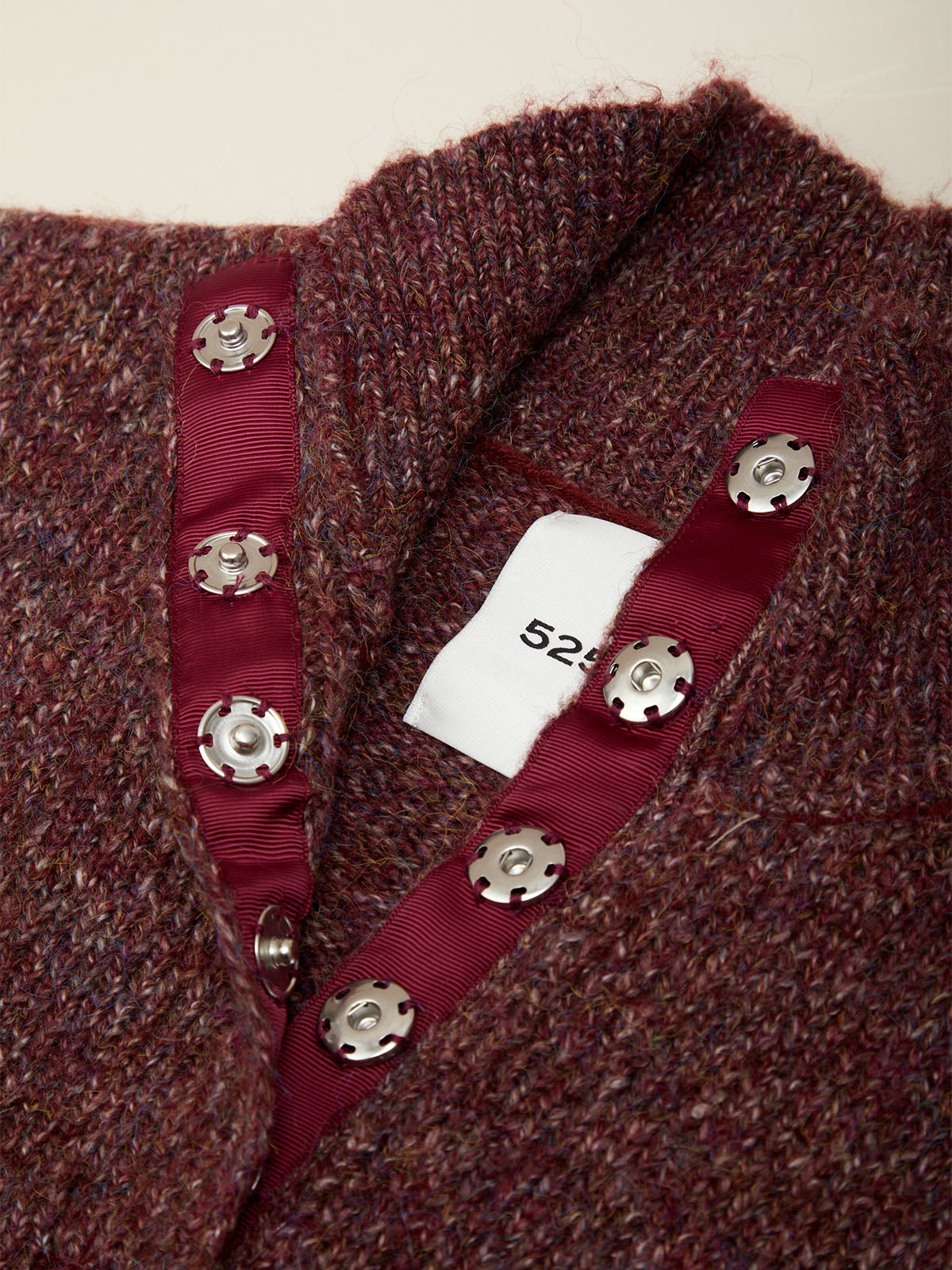 Close-up of a textured maroon knit sweater with a burgundy ribbon trim and decorative silver-tone buttons, showing a white size tag with the number 52.
