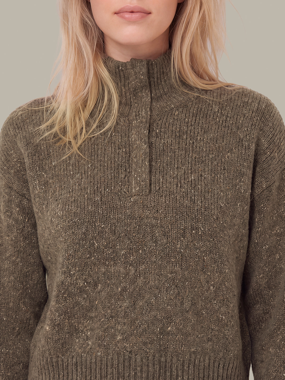 A close-up of a woman wearing a ribbed knit mock-neck sweater in a heathered brownish-gray color with subtle flecks.