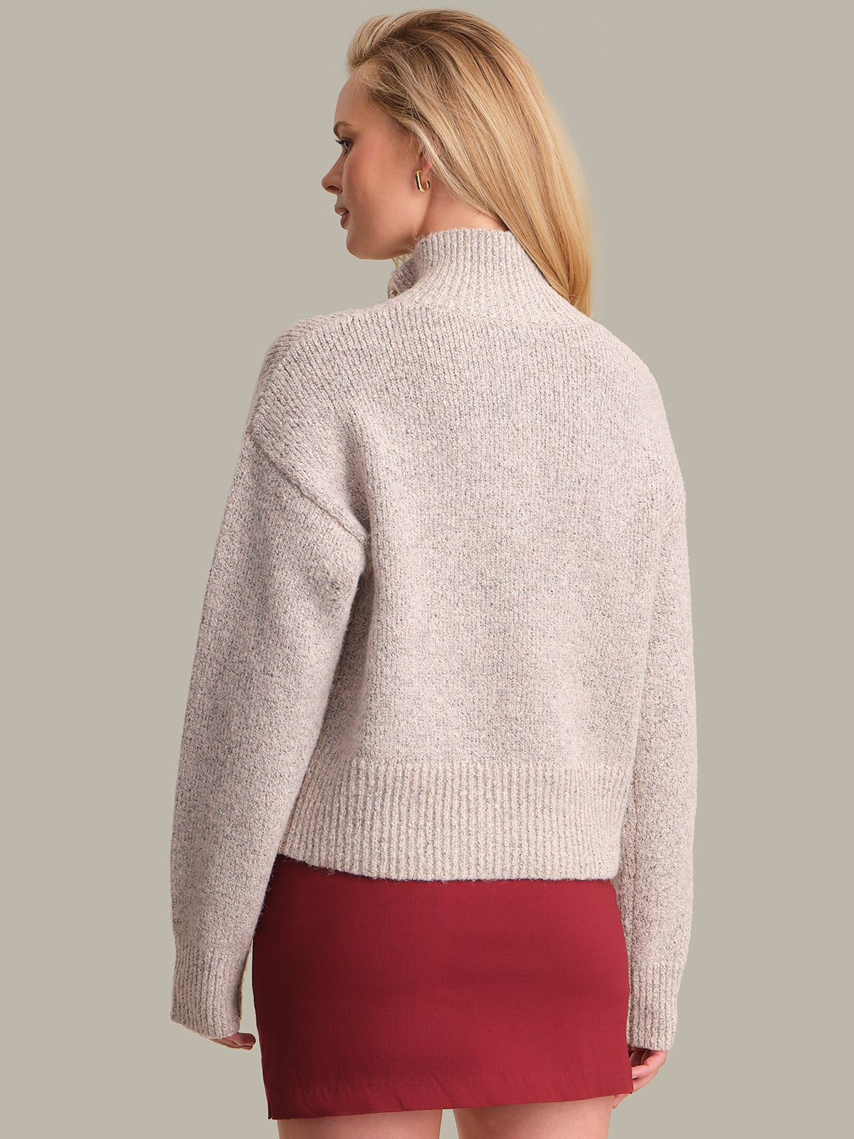 Woman wearing a beige knitted sweater and red skirt on a plain background