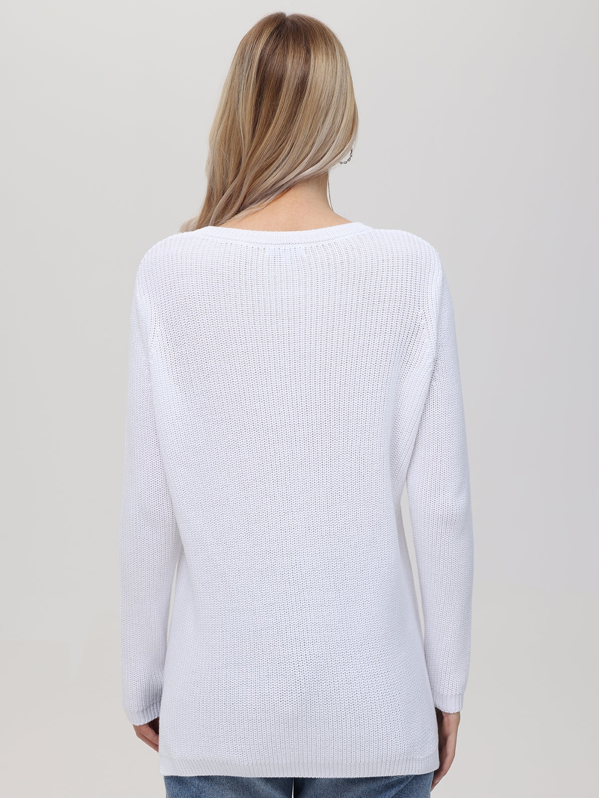 A person with long, light brown hair is seen from behind wearing a 525 America white long-sleeve shaker stitch knit sweater and blue jeans, standing against a plain light grey background.