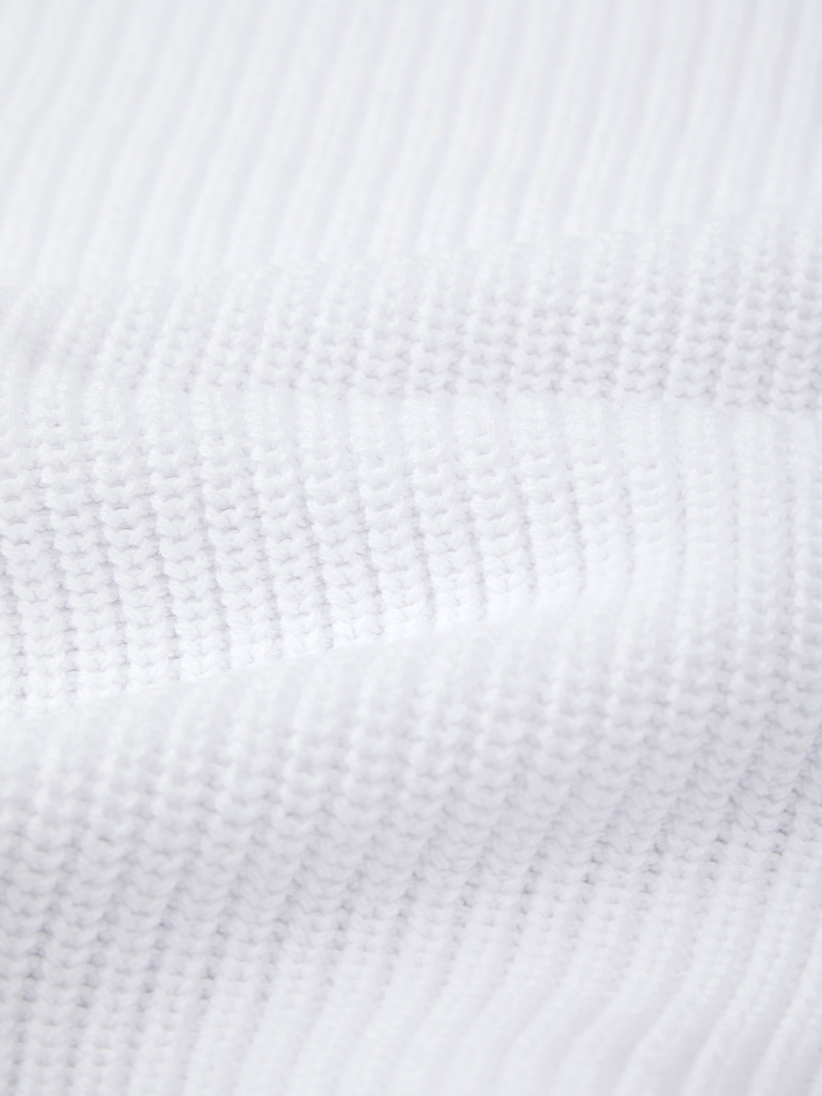 Close-up of a white, ribbed shaker stitch fabric by 525 America, featuring visible horizontal and vertical ridges. Made from 100% cotton, its raised texture appears soft with lighting accentuating the details.