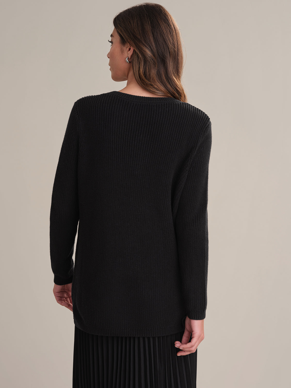 Person wearing a black sweater and skirt set against a neutral background