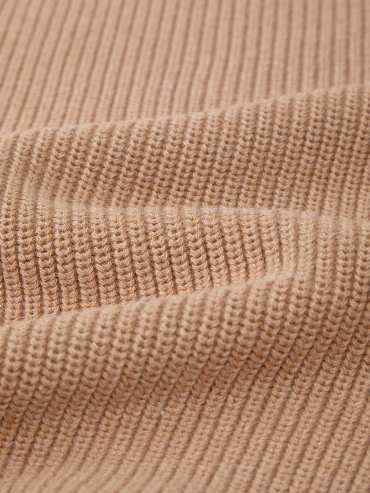 Close-up of a beige, ribbed knitted fabric by 525 America in versatile shaker stitch, highlighting visible texture, horizontal ridges, and soft folds with detailed yarn pattern.