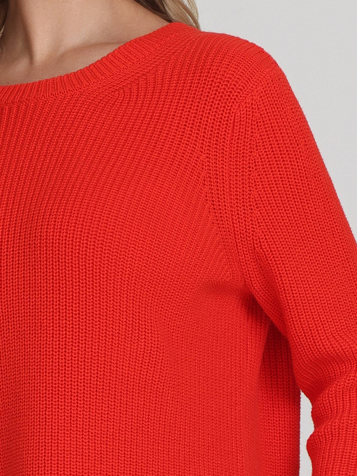 A person is seen in a bright red, long-sleeved knitted sweater by 525 America. The sweaters versatile style and relaxed fit are highlighted by its shaker stitch texture. Wisps of hair drape over their shoulder, subtly contrasting with the cozy fabric.