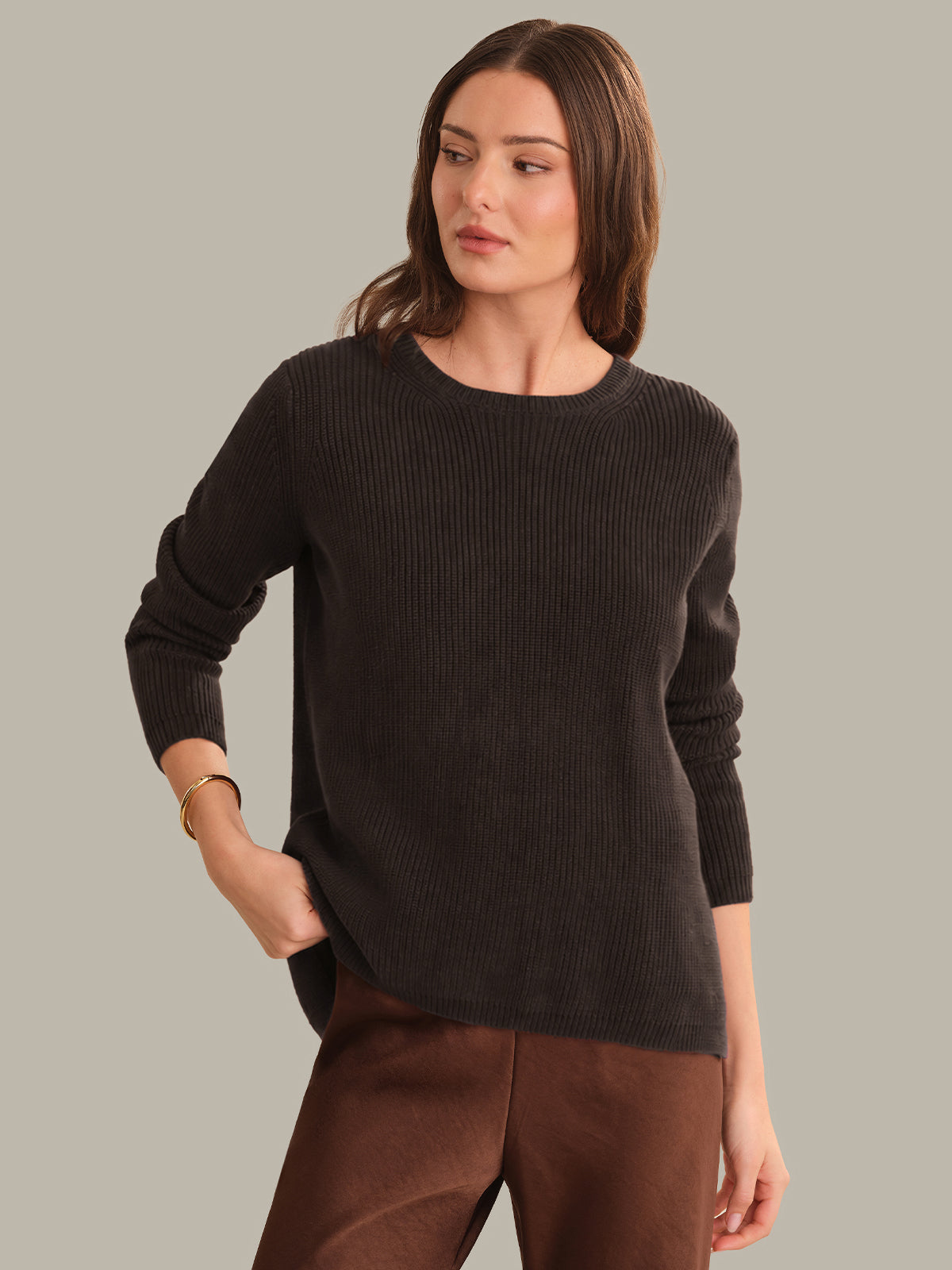 Woman wearing a dark brown sweater and brown pants against a gray background