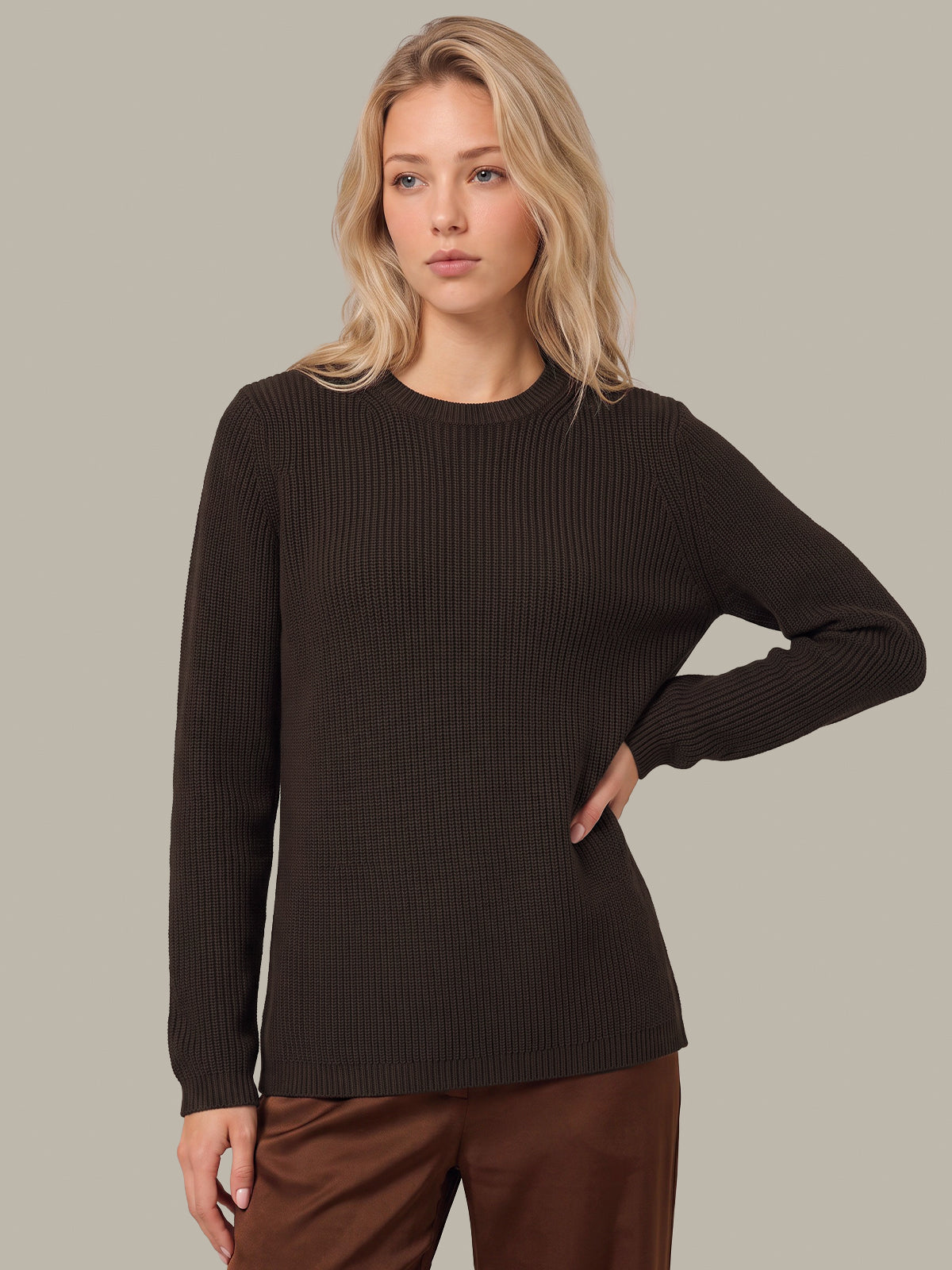 A woman modeling a dark brown ribbed knit long-sleeve sweater against a solid light gray background.