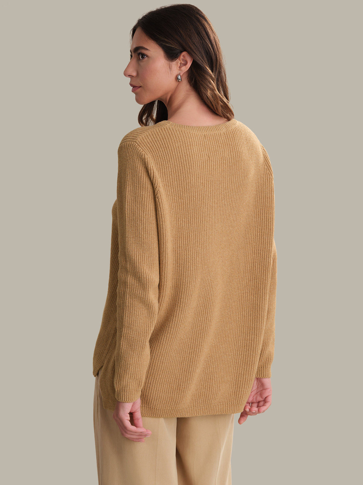 Woman wearing a mustard yellow sweater and pants against a neutral background