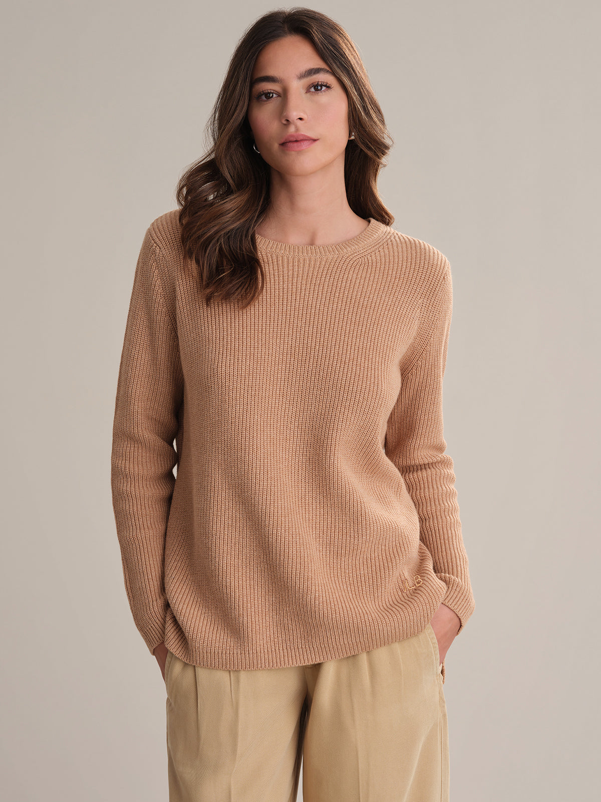 Woman wearing a beige sweater and pants against a neutral background
