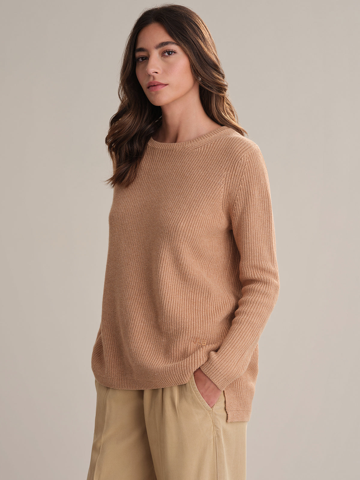 Woman wearing a beige sweater and pants against a neutral background