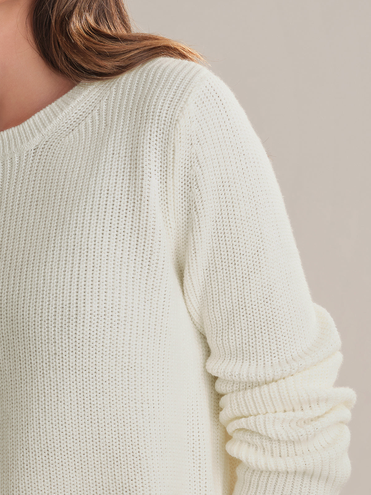 Close-up of a person wearing a white sweater against a neutral background
