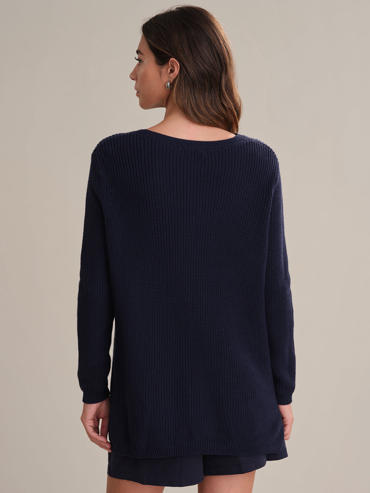 Woman wearing a navy blue sweater and shorts on a beige background