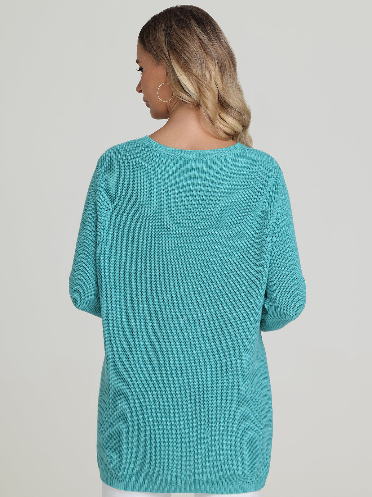 A person with long hair faces away from the camera, wearing a turquoise knitted sweater by 525 America. The chic, shaker stitch design offers a relaxed fit and adds texture against the light backdrop.