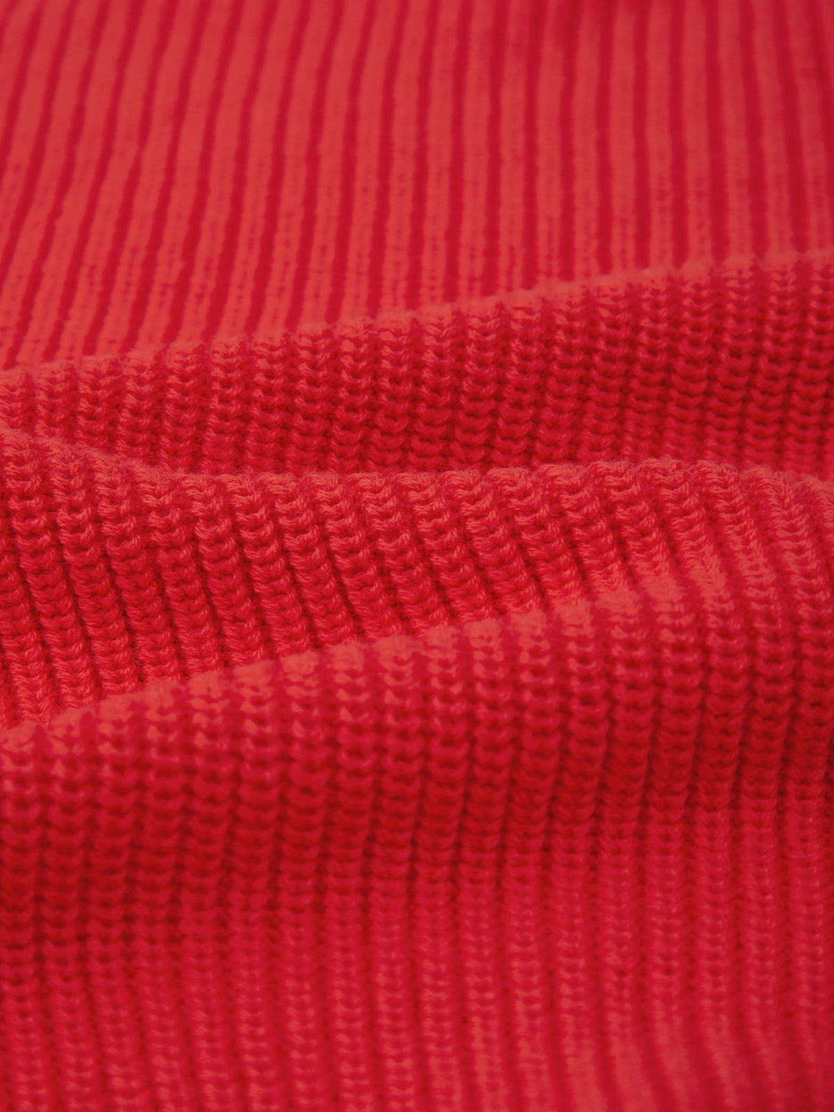 Close-up of red ribbed knit fabric from 525 America with horizontal ridges and visible texture. Crafted from 100% cotton, the material looks soft and slightly stretched, showing raised lines and subtle shadows between folds.