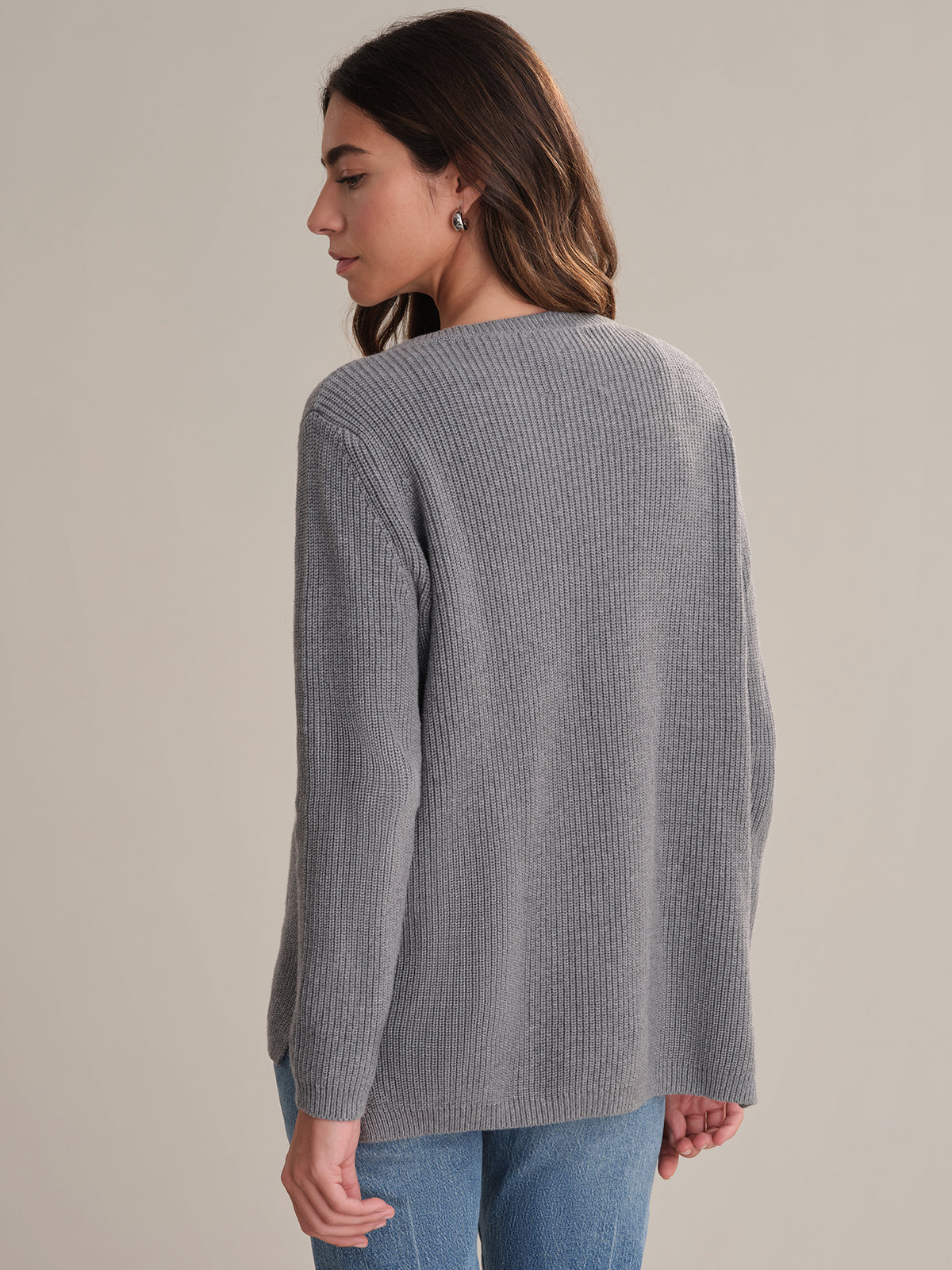 Woman wearing a gray ribbed sweater and blue jeans on a plain background