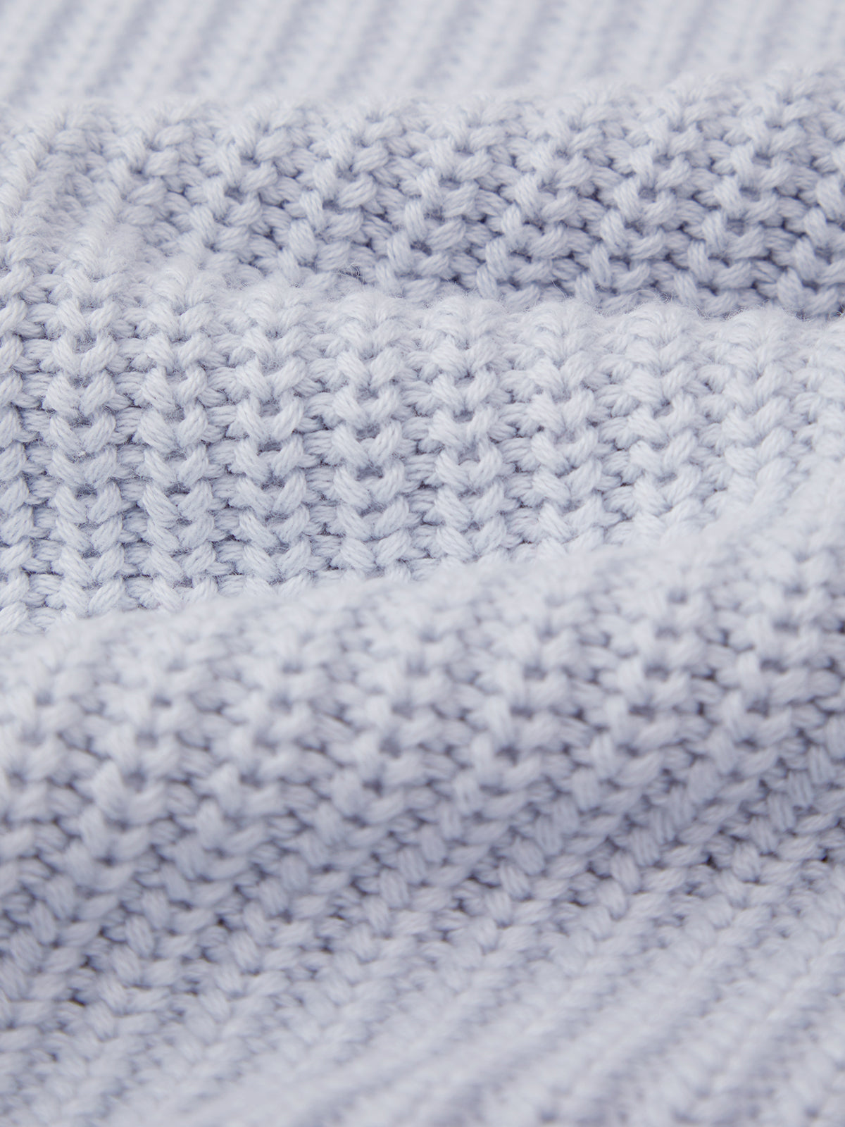 Close-up view of a 525 America light gray cotton shaker stitch sweater with ribbed texture, detailed stitches, and soft, wavy folds.