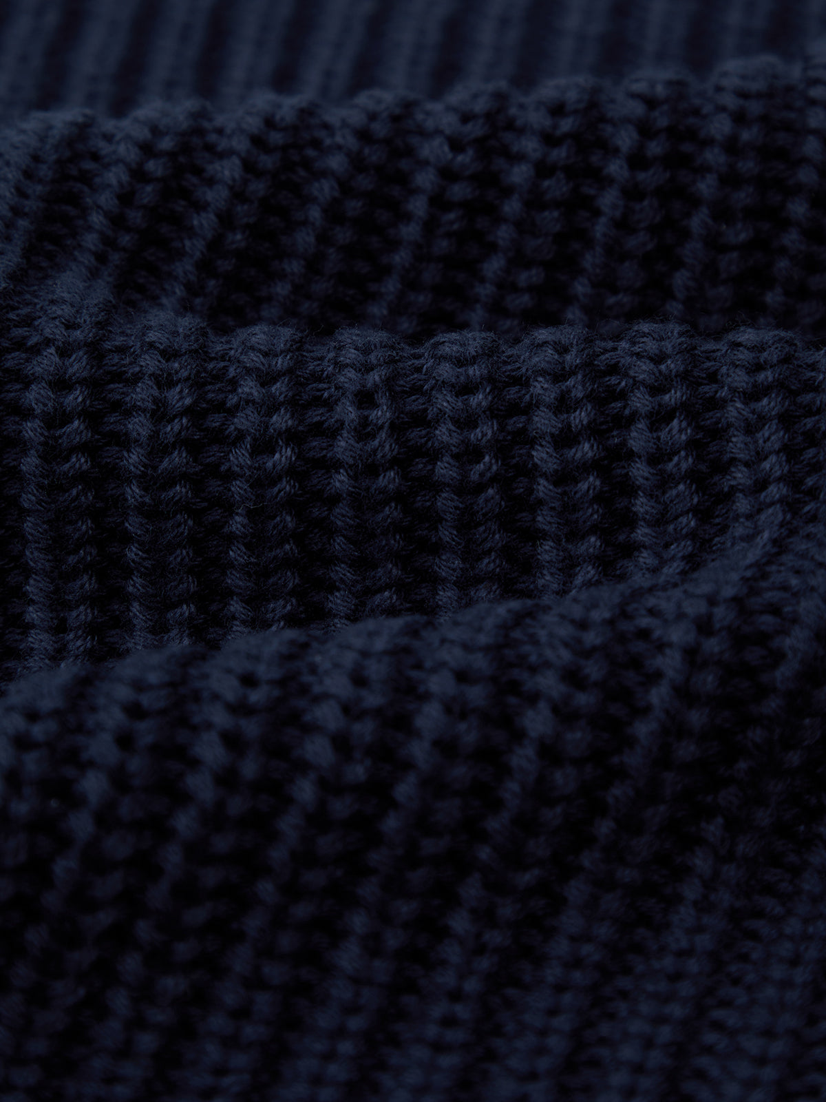 Close-up of dark navy blue ribbed knit fabric from a 525 America cotton shaker stitch sweater, highlighting its textured pattern and fine stitching details.