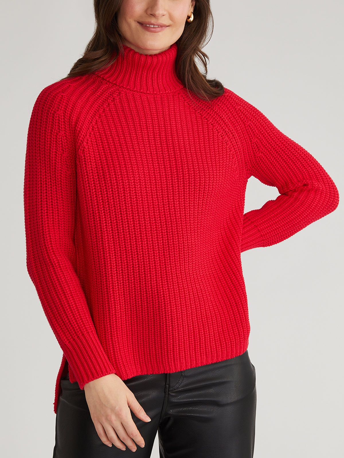 Wearing a cozy 100% cotton bright red turtleneck sweater by 525 America and black leather pants, the person stands with one hand on their hip against a plain gray background.