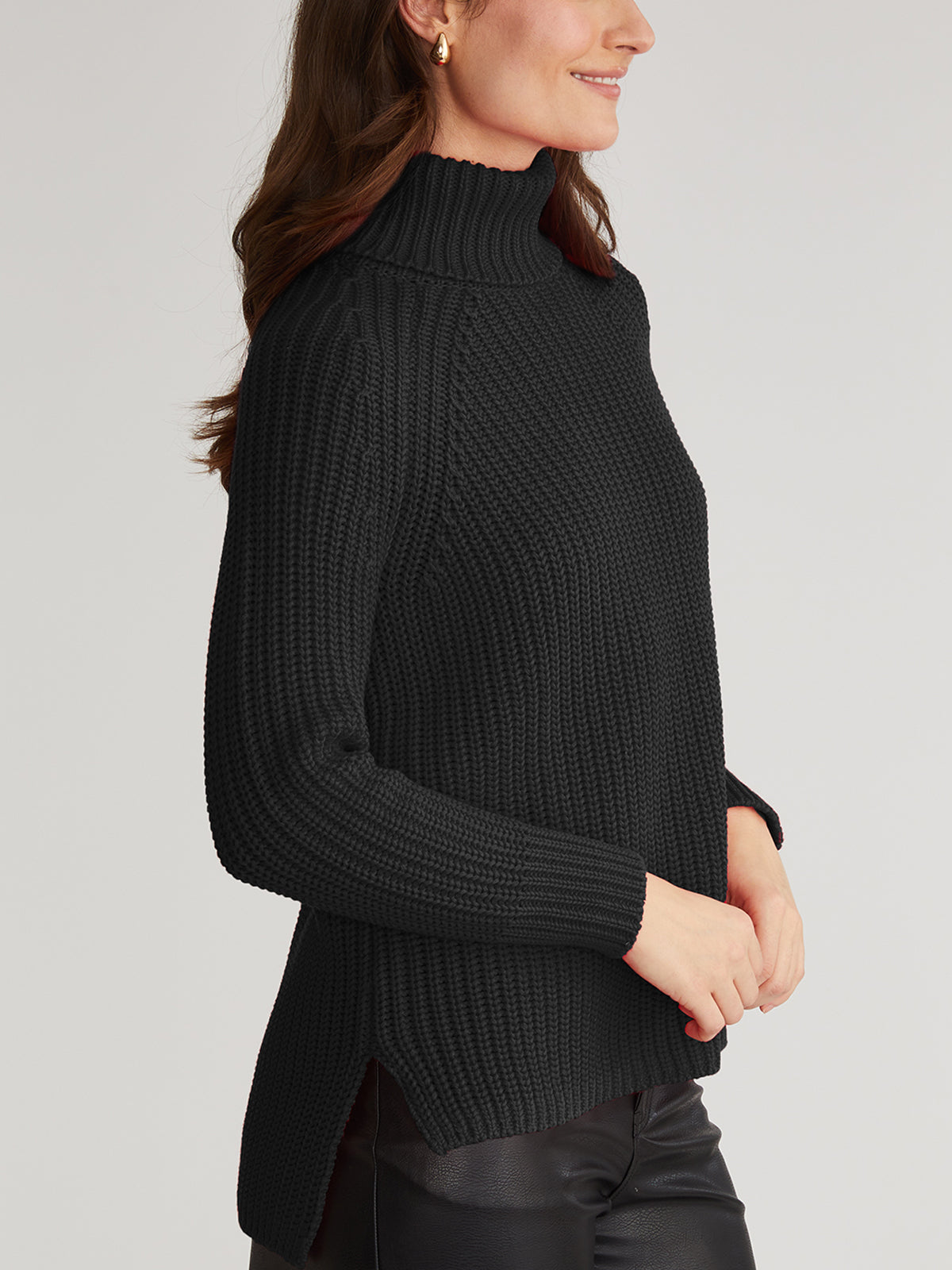 The individual is shown in a cozy black ribbed turtleneck sweater from 525 America and sleek leather pants, captured in side profile. The 100% cotton high-neck, long-sleeve sweater perfectly complements their long brown hair and slight smile.