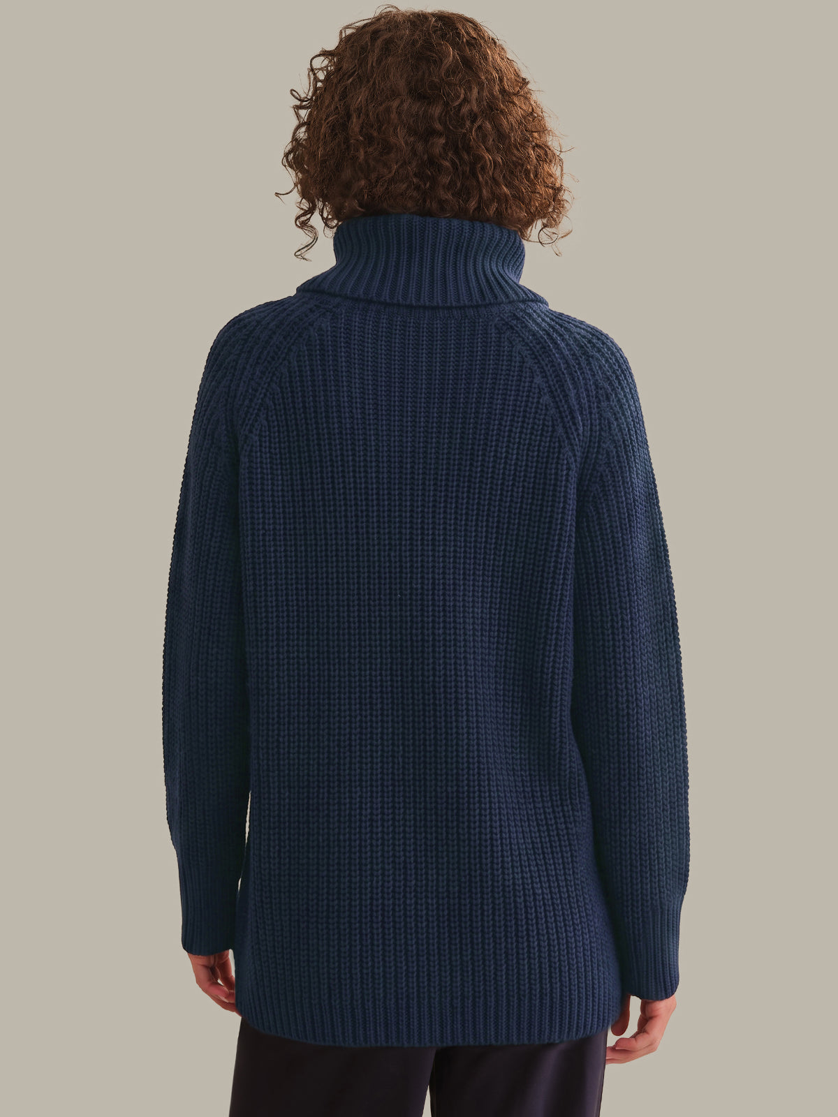 Person wearing a blue ribbed sweater against a plain background