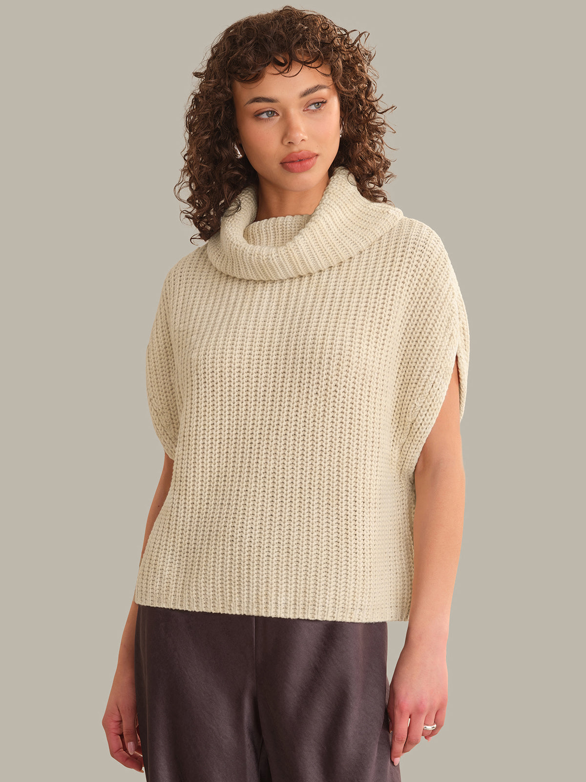 Woman wearing a beige knitted sleeveless sweater against a neutral background