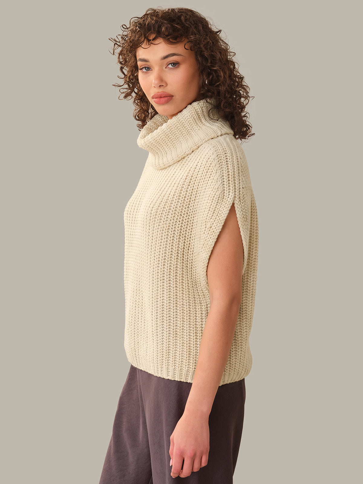 Woman wearing a beige knitted vest against a plain background