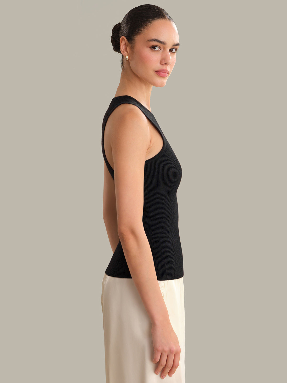 Woman wearing a black sleeveless top and white pants against a gray background