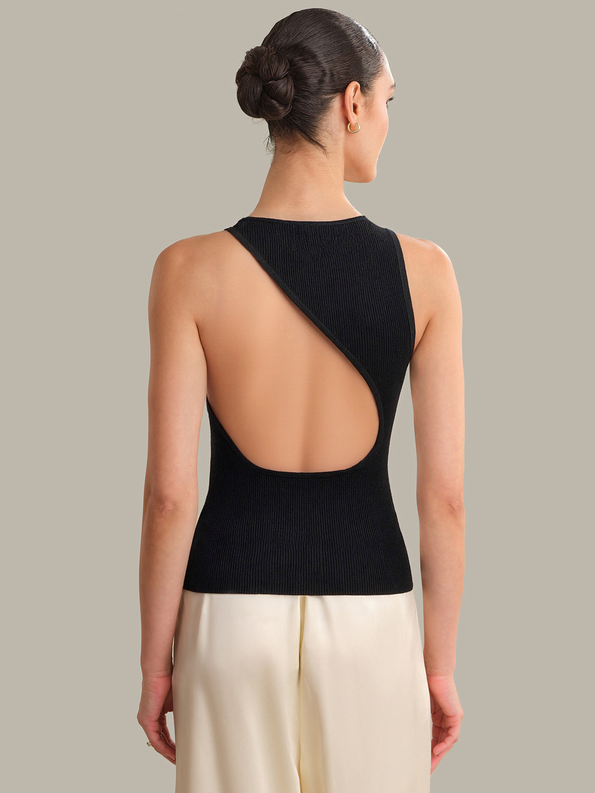Woman wearing a black open-back top and beige pants against a neutral background