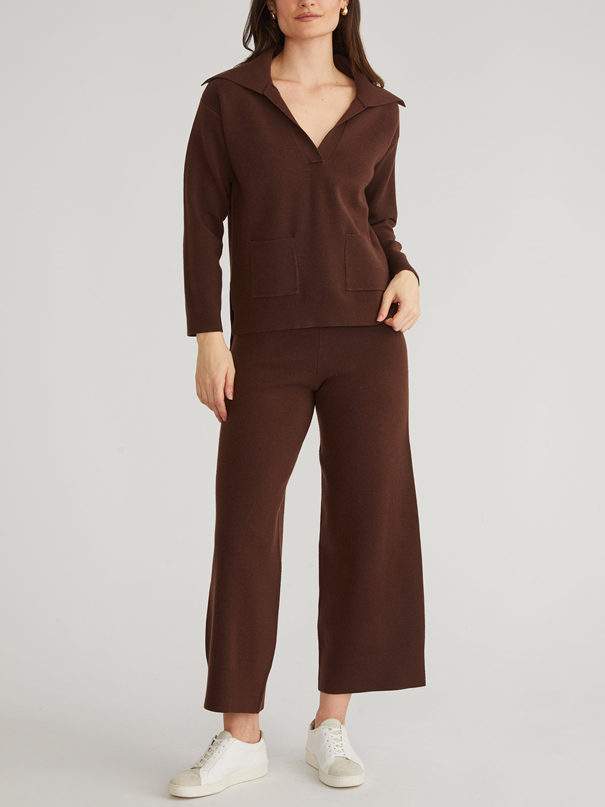 A person stands against a plain backdrop, showcasing their winter wardrobe with a trendy brown long-sleeve Sailor Collar Pullover and matching wide-leg pants from 525 America. Completing the look are white sneakers, with their right hand casually in a pocket.