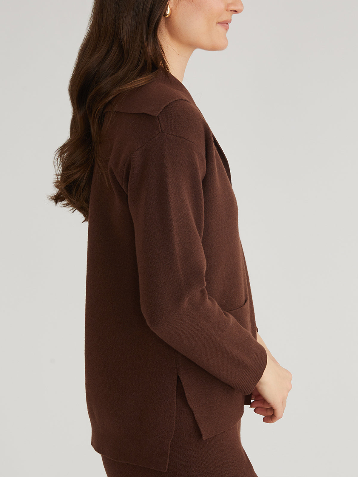 A person with long brown hair wears a matching brown blazer and pants from 525 America, in profile against a plain white background—adding a trendy piece to elevate any winter wardrobe.