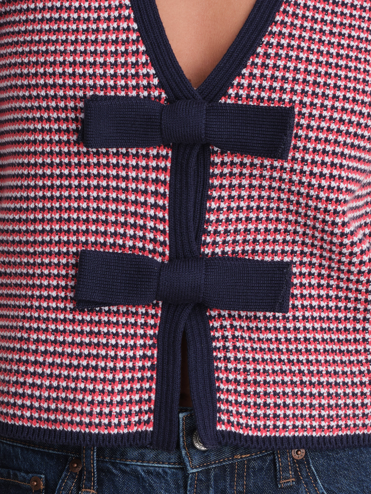 A close-up of a 525 America feminine cardigan with a red, white, and blue checked pattern, featuring two large navy bow ties on the front and blue denim jeans visible at the bottom.